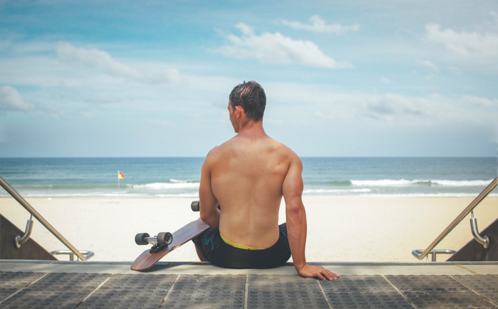 man sitting on gray surface holding skateboard