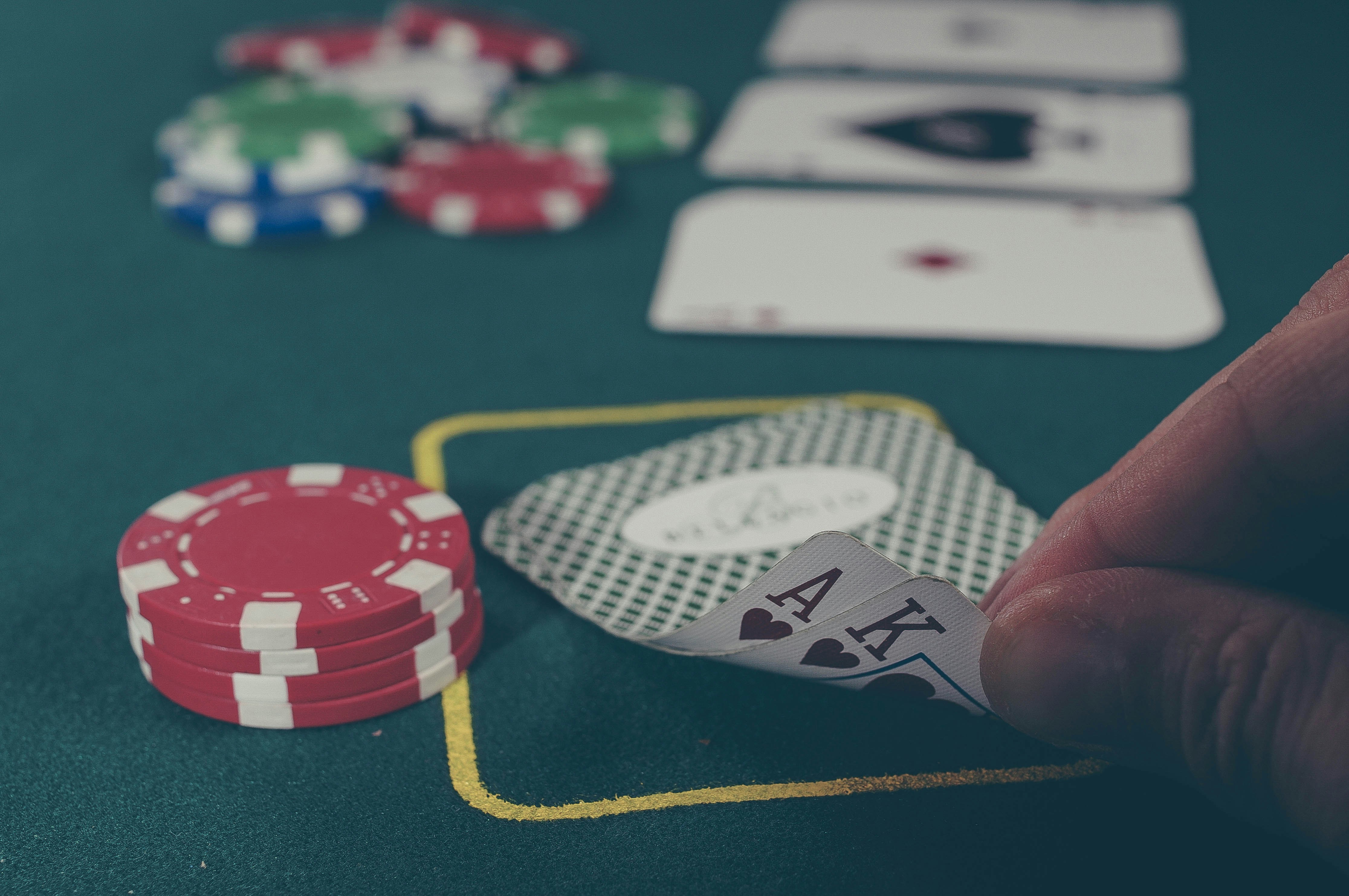 Image shows a poker table with fingers holding a card and some playing pieces