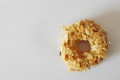 A donut covered with a generous amount of sliced almonds is placed against a plain background. The icing beneath the almond slices appears to be a light color, possibly a vanilla glaze.