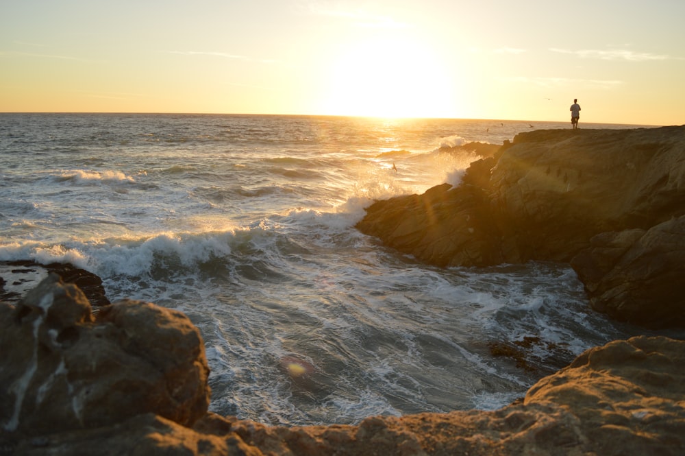 person on rock formation during sunset