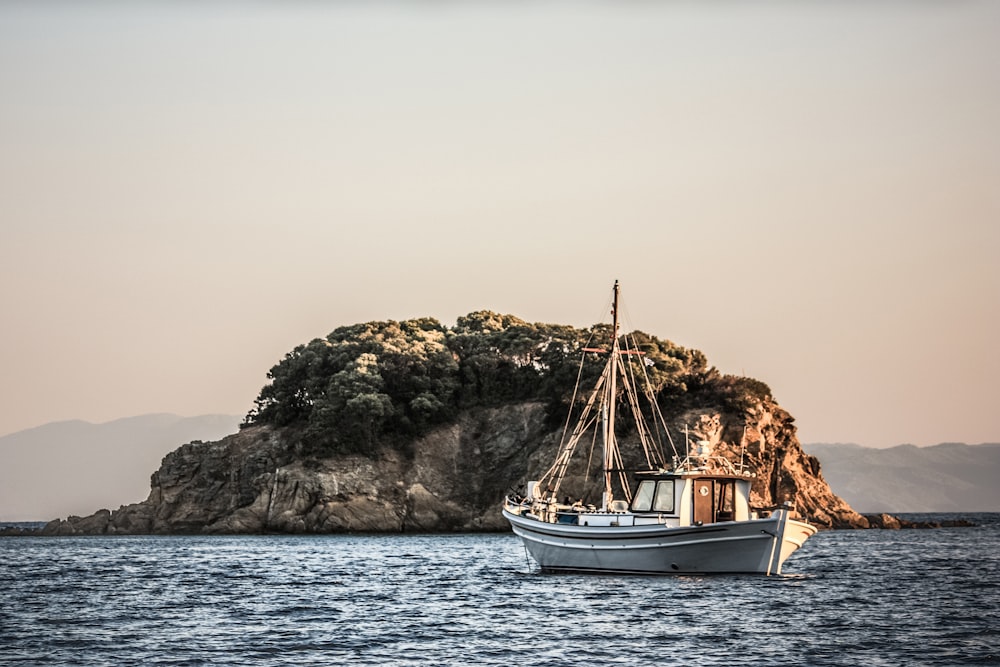 white boat near brown and green mountain by the sea during daytime