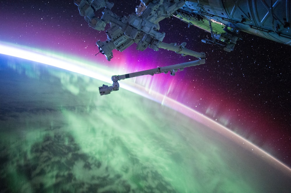 Photographie d’un faisceau d’aurores violettes et vertes sous un satellite spatial gris