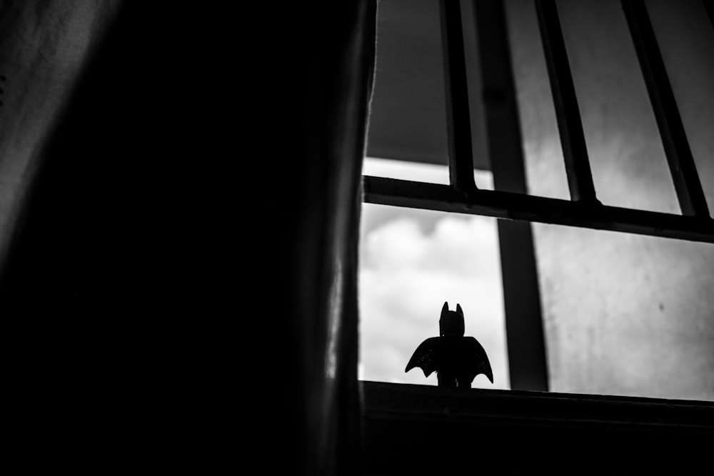 A Lego Batman toy sitting in a window looking out to the sky.