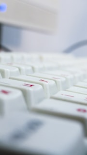 A close-up view of a white keyboard with some red symbols on the keys, featuring a blurred depth of field effect and a soft, cool-toned lighting.