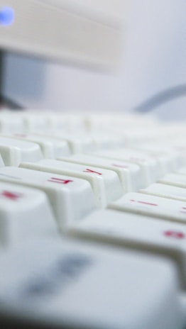 A close-up view of a white keyboard with some red symbols on the keys, featuring a blurred depth of field effect and a soft, cool-toned lighting.
