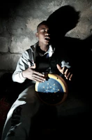 A drummer deeply focused, eyes closed, feeling the rhythm surrounded by shadows and warm light.