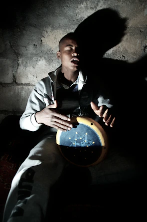 A drummer deeply focused, eyes closed, feeling the rhythm surrounded by shadows and warm light.