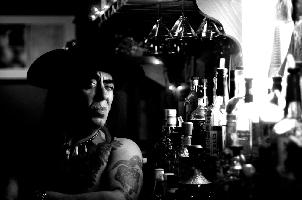 man wearing hat beside bottles on grayscale photography