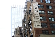 A juxtaposition of an older, brick office building with a large advertisement for business space, and a modern, sleek glass skyscraper in the background. The older building features multiple windows and a vintage sign promoting Adams & Co. Real Estate at 411 5th Ave.