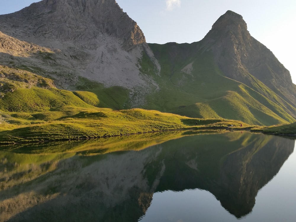 green mountain near lake under white cloudy sky