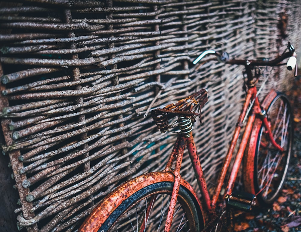 red bicycle parked beside brown wood wall at daytime