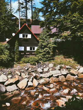 A cozy red sandalwood house nestled among lush greenery at sunset.