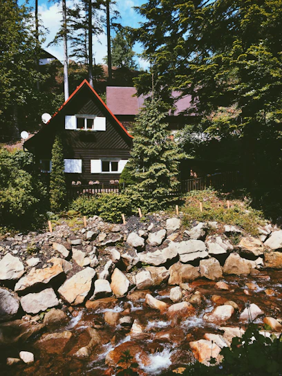 A cozy red sandalwood house nestled among lush greenery at sunset.