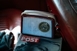 A vintage radio with a central tuning dial rests on a leather seat. Next to it lies a magazine with a partial cover image of a woman's face and the title 'PICTURE POST' in bold red letters, creating a nostalgic ambiance.