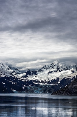 calm lake water near snowy mountain peak under cloudy skies