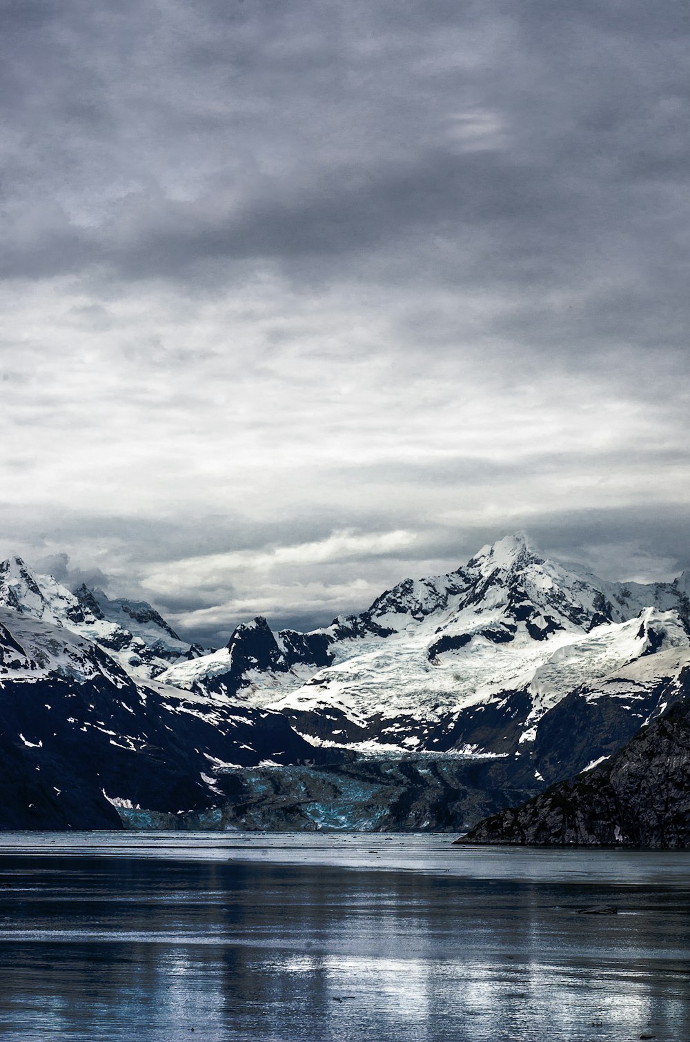 Acqua calma del lago vicino al picco nevoso della montagna sotto i cieli nuvolosi