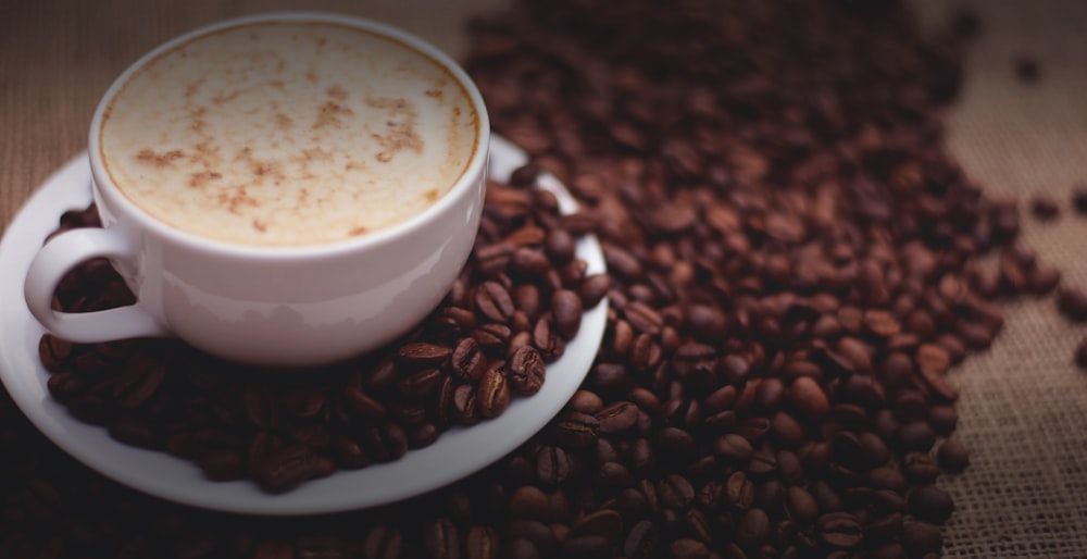 filled white cup on top of white saucer surrounded by coffee beans