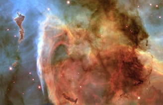 A stunning cosmic scene featuring swirling clouds of colorful gas and dust, with bright stars scattered throughout the space. The image has a mix of brilliant blues and fiery oranges, creating a vibrant and dynamic composition. Patterns of dark shadows interplay with lighter areas, giving a sense of depth and mystery to the scene.