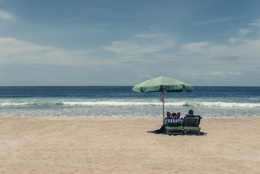 people sitting on seashore under green umbrella during daytime