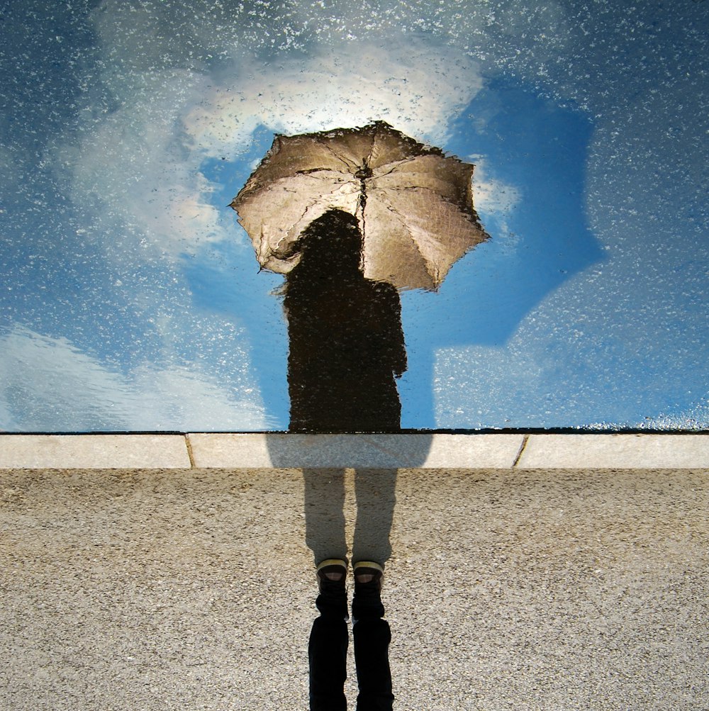 Persona de pie sobre una superficie gris mientras sostiene un paraguas
