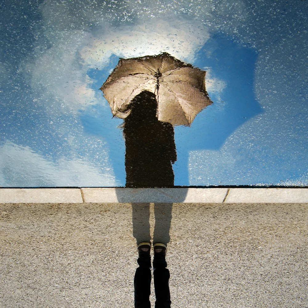 pessoa em pé na superfície cinza enquanto segura o guarda-chuva