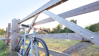 A rustic bicycle leaning against a weathered wooden fence on a sunlit country road.