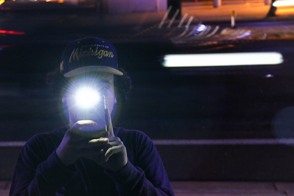 User holding an iPhone with FlashGlow app active, casting a bright torch beam outdoors at night.