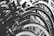 A close-up view of a row of bicycle wheels, focusing on the tires and rims. The image is in black and white, emphasizing the texture and symmetry of the repeating circular patterns.