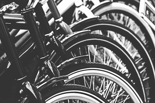 A close-up view of a row of bicycle wheels, focusing on the tires and rims. The image is in black and white, emphasizing the texture and symmetry of the repeating circular patterns.