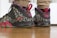 A pair of stylish sneakers featuring a black and speckled design with red accents. The sneakers include prominent branding and are worn by someone standing on a wooden floor.