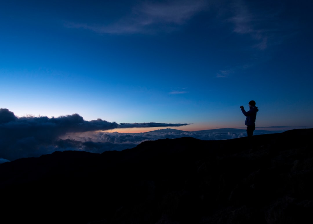 silhouette of man taking photo on rock cliff