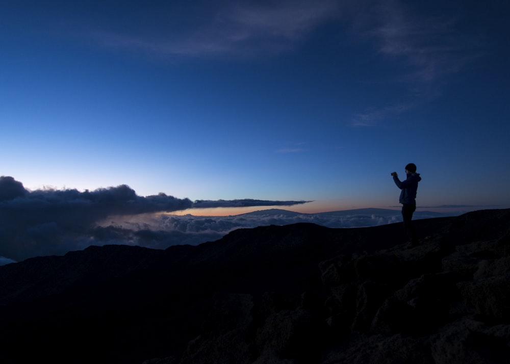 silhouette of man taking photo on rock cliff