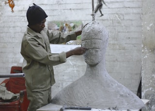 A sculptor works in his studio sculpting a large white body and head