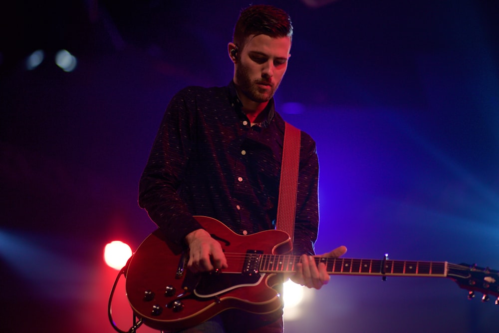 A male guitarist in a shirt performing on stage with blue and red lights behind him