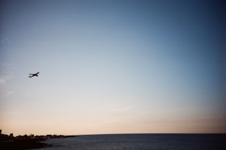 A bright airplane flying over a clear blue ocean with Miami's coastline in the background.