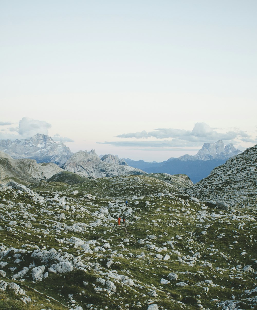 two people walking on hill under cloudy sky