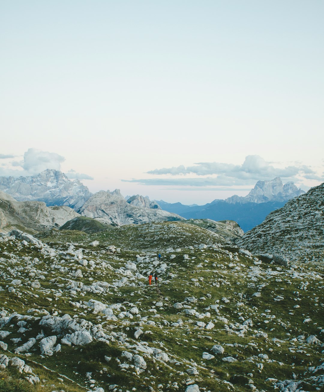 two people walking on hill under cloudy sky