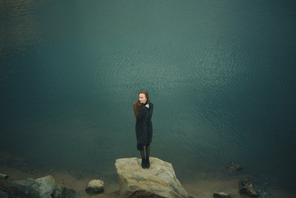 Mujer de pie sobre una gran roca gris a lo largo del cuerpo de agua