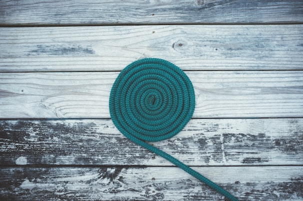 A vibrant custom biothane lead in teal and orange, coiled neatly on a wooden table.