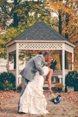 groom kissing bride near white gazebo