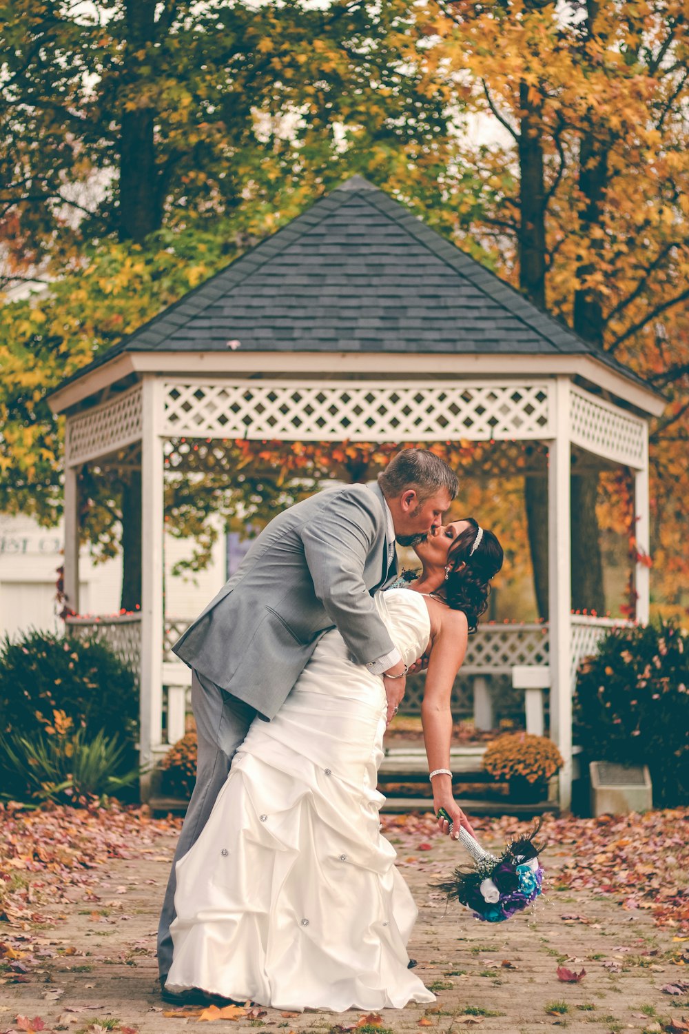 groom kissing bride near white gazebo