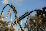 A thrilling roller coaster twisting high above a lush green forest under a bright blue sky.