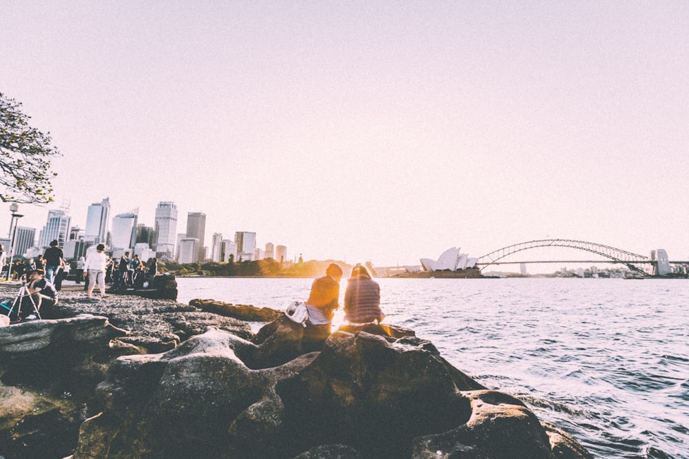 personnes assises et debout sur le rivage regardant le coucher de soleil près de l’Opéra de Sydney en photographie panoramique