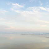 Wide-angle shot of a calm beach with soft pastel skies.
