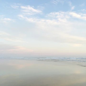 Wide-angle shot of a calm beach with soft pastel skies.