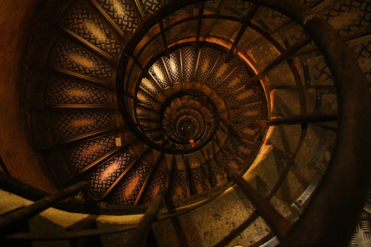 A spiral staircase photographed from directly below, centred precisely so the repeating steps lead the eye into the circle of light.