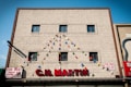 A beige building facade with four small windows displays the name 'C.H. MARTIN' in large red letters. Colorful triangular pennant flags are strung above, forming a festive appearance. Two 'FOR RENT' signs are visible on either side of the building.