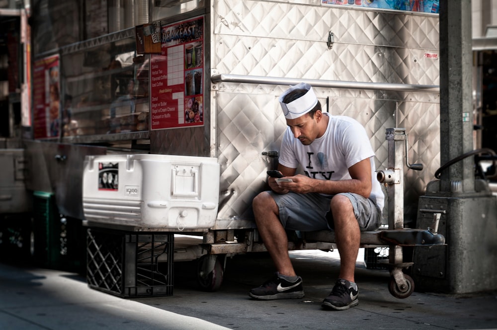 hombre con camisa blanca sosteniendo un teléfono inteligente sentado cerca de la nevera del pecho