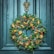 A decorative holiday wreath is adorned with pinecones, dried orange slices, cinnamon sticks, and red berries. It hangs on a dark teal wooden door with a detailed brass door knocker depicting a face.