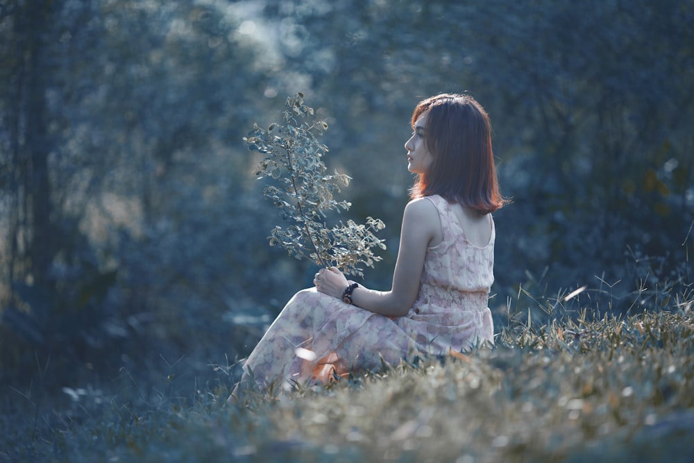 A woman sits on a grassy hill holding a tree branch in tp. Pleiku